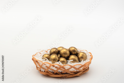 Golden chocolate Easter eggs in egg basket with white paper like a nest. Happy Easter holiday concept. Banner with copy space.