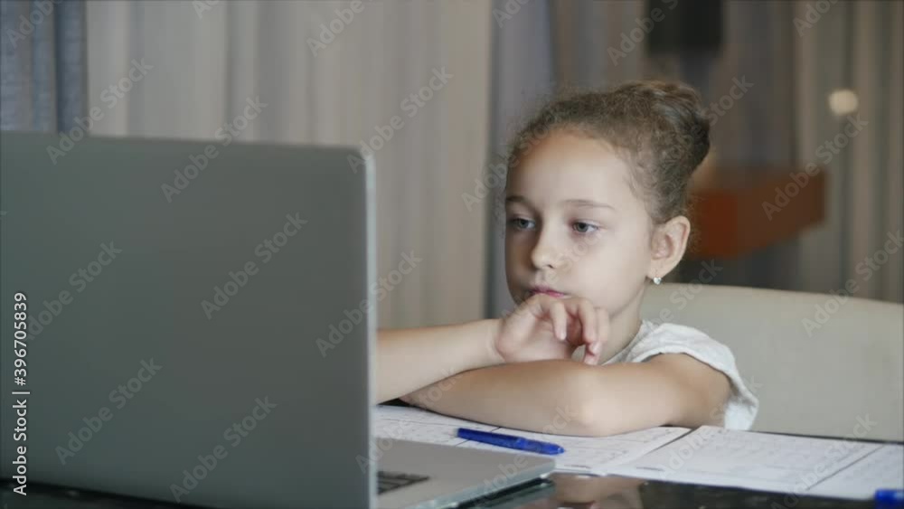 The younger student sits at home at the computer, studies, listens to school lectures, and does his homework at home. Children at home, family education, children education concept. The younger student sits at home at the computer, studies, listens to school lectures, and does his homework at home. Children at home, family education, children education concept.