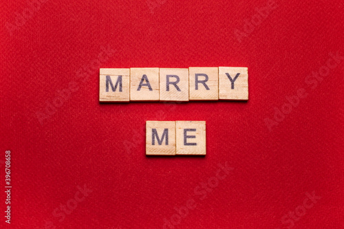 Wooden block lettering "marry me" on red textured background: wedding background, top view, minimalism