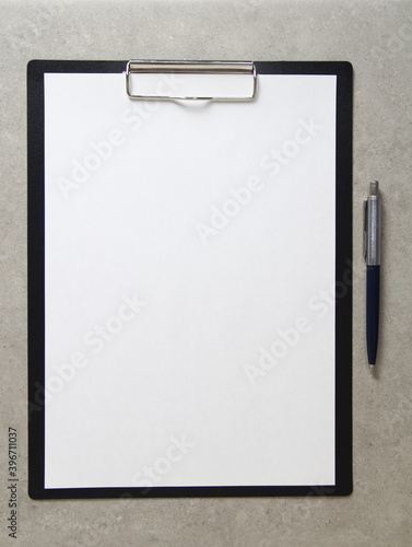 Template of white paper with a ballpoint pen on light grey concrete background in a black tablet with a clip. Concept of new idea, business plan and strategy, with empty space for text