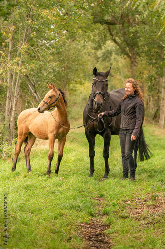 Happy smiling woman next to her horse and foal in the forest. Autumn colors © Dasya - Dasya
