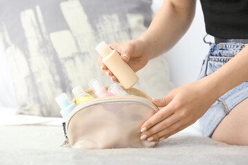 Woman and bag with travel bottles with body care cosmetics on light background