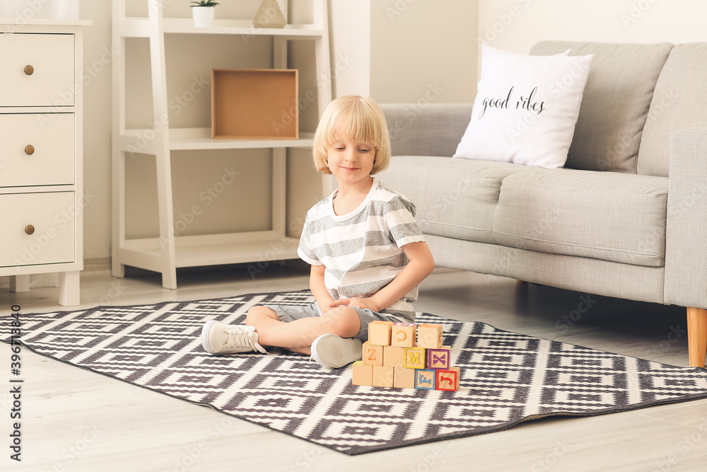 Cute little boy playing with wooden cubes on carpet at home Cute little boy playing with wooden cubes on carpet at home