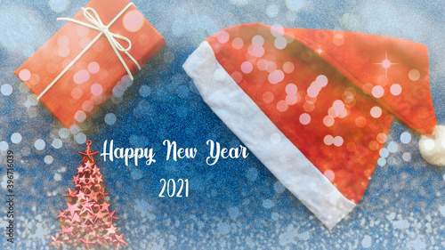New Year concept. Santa Claus hat, gift, toy tree on a blue glitter background with the inscription.