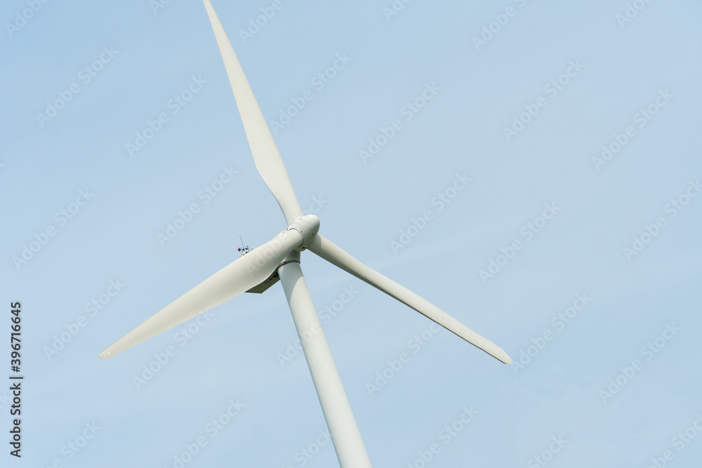 view of a modern windmill against a blue sky. The white blades of the wind turbine. Wind turbines in the forest away from the big city on a summer day. Clean and renewable energy production view of a modern windmill against a blue sky. The white blades of the wind turbine. Wind turbines in the forest away from the big city on a summer day. Clean and renewable energy production