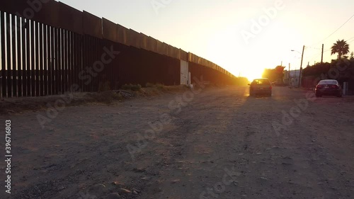 A large car speeds up and drives into toward the rising sun along the ever contentious U.S.-Mexico border on the Mexican side, kicking up a proverbial cloud of dust which lingers in the golden light.