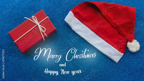 Santa Claus hat and New Years gift on blue glittering New Years background. Merry Christmas lettering. New Year concept