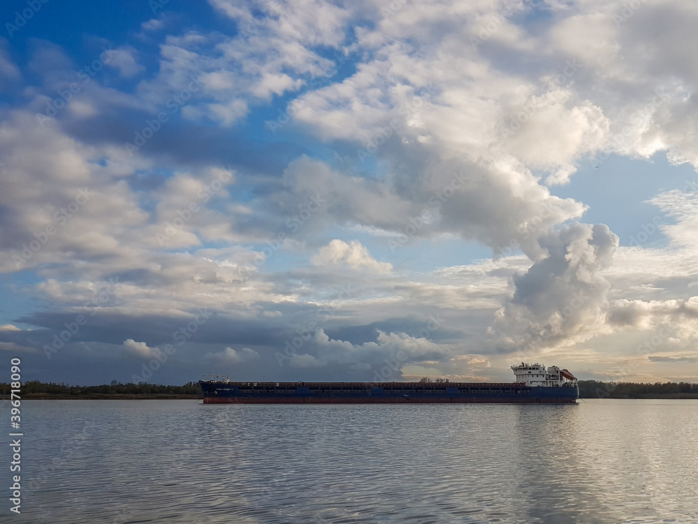 Cargo ship in river under blue sky with cumulus clouds