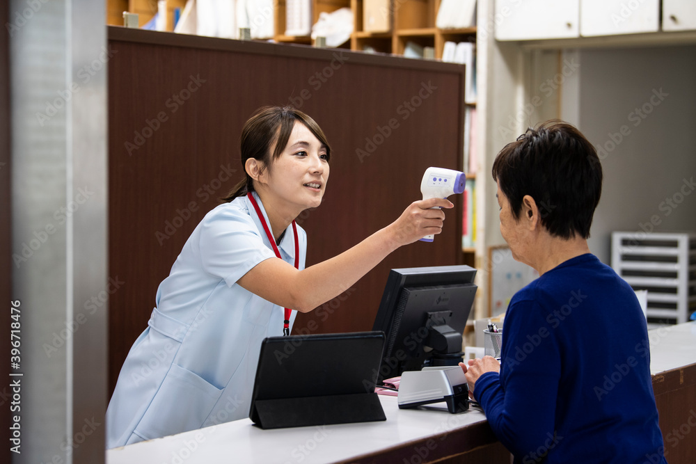 病院の受付で患者の体温を測る看護師 病院の受付で患者の体温を測る看護師