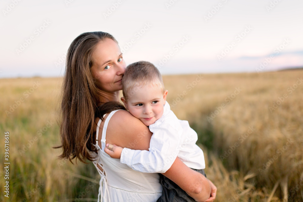Caucasian beautiful mother hugs her child son in the summer wheat field at sunset, summer and harvest, natural products and relaxation in the countryside, motherhood Caucasian beautiful mother hugs her child son in the summer wheat field at sunset, summer and harvest, natural products and relaxation in the countryside, motherhood