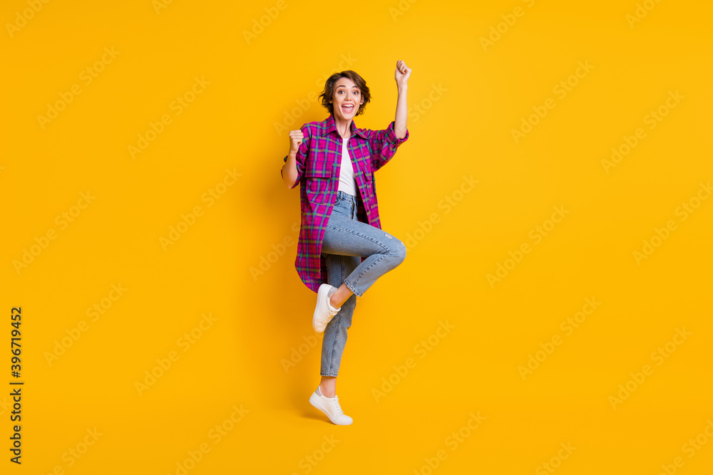Full length photo charming girl pose win raise fists yes wear jeans plaid shirt isolated on yellow color background Full length photo charming girl pose win raise fists yes wear jeans plaid shirt isolated on yellow color background