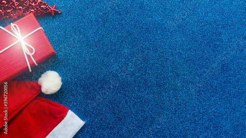 Christmas background. Santa Claus hat, gift, toy tree on blue glitter background. View from above