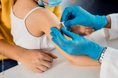 Close-up of doctor placing adhesive bandage on little girl's arm after vaccination.