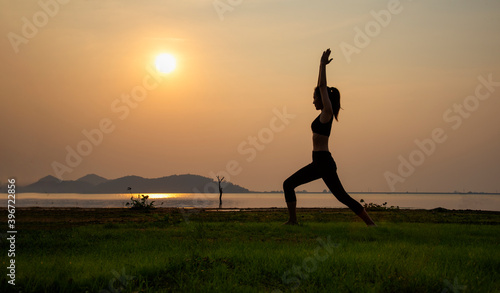 young woman practicing yoga or fitness at seashore at sunset in the nature