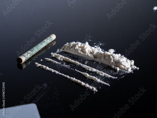 Lines of cocaine and a dollar bill. Cocaine lines shots on a black table glass. Cocaine powder, Credit card, close up, toned. Drug abuse concept. White poder on black table