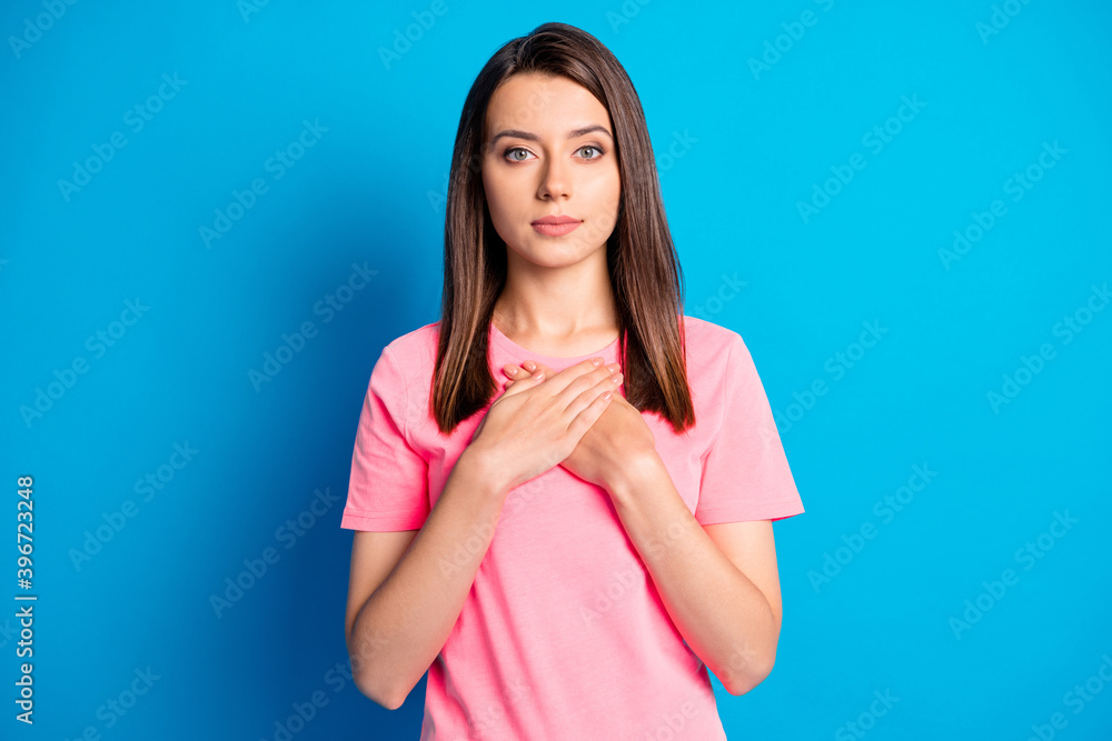 Photo portrait of calm girl keeping hands on chest wearing pink outfit isolated on vibrant blue color background Photo portrait of calm girl keeping hands on chest wearing pink outfit isolated on vibrant blue color background
