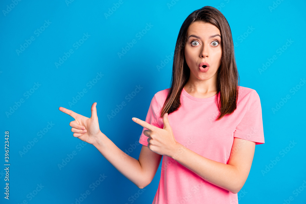 Photo portrait of amazed shocked girl staring opened mouth pink t-shirt pointing at blank space isolated on vivid blue color background Photo portrait of amazed shocked girl staring opened mouth pink t-shirt pointing at blank space isolated on vivid blue color background