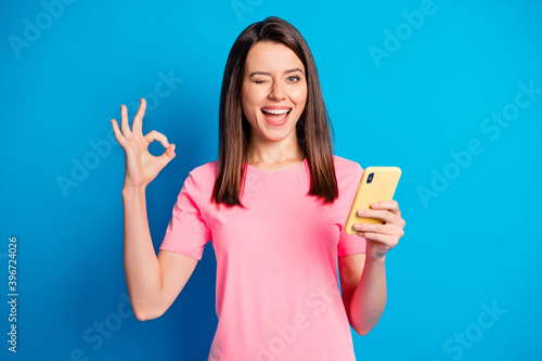 Photo of funny attractive lady eye wink fingers show okey symbol pink t-shirt isolated on blue color background © deagreez