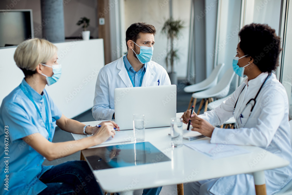Group of healthcare experts with face masks talking during a meeting at medical clinic. Group of healthcare experts with face masks talking during a meeting at medical clinic.