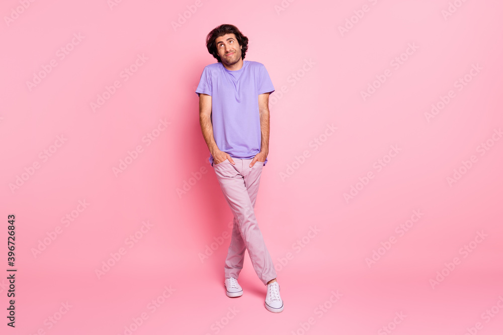 Full length photo of shy man look up empty space wear violet t-shirt pants footwear isolated pastel pink color background Full length photo of shy man look up empty space wear violet t-shirt pants footwear isolated pastel pink color background