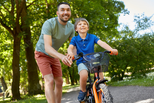 family, fatherhood and leisure concept - happy father teaching little son to ride bicycle at park