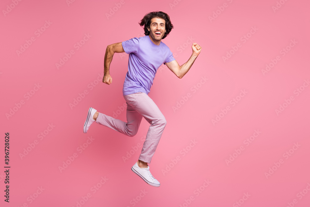 Full body photo of joyful brown haired young man jump run in air wear pink pants violet t-shirt isolated on shine pastel pink color background Full body photo of joyful brown haired young man jump run in air wear pink pants violet t-shirt isolated on shine pastel pink color background