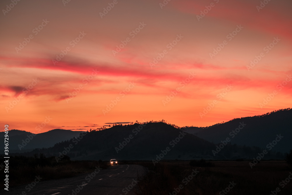 The car moves on the road against the background of mountains and sunset