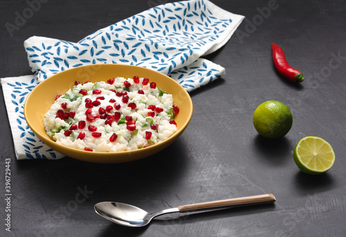 Traditional curd rice in a yellow plate on a dark background. Spoon, lime, hot red pepper, and white napkin.