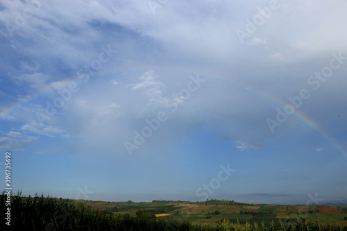 A half-circle rainbow occurs in rural farmland.