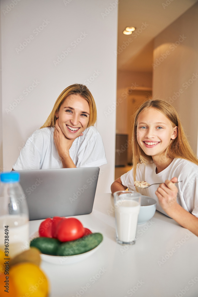 Smiling girl and her freelancer mother at breakfast Smiling girl and her freelancer mother at breakfast