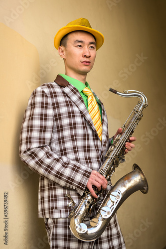 Asian guy with saxophone standing against a wall