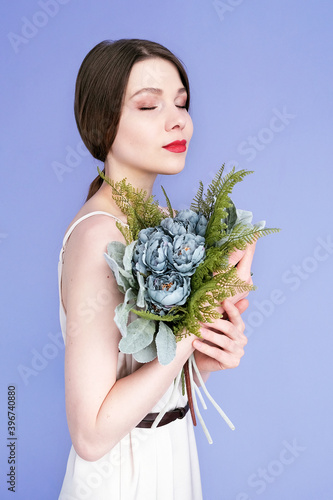Girl with a bouquet isolated on a purple background. A girl with red lips and closed eyes is holding a bouquet of flowers.