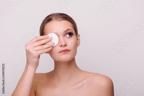 Beautiful girl removes makeup. Cleansing the skin from evening make-up. Cotton pads and tonic. Cosmetics remover. Isolate background copy-space for text. Close-up portrait. Purity face. hygiene