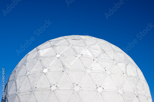 Abandoned dome of an old Soviet military radar from the Cold War. A huge structure in the form of a white sphere against a blue sky. Fragment of a spherical dome close-up. Top of a large structure.