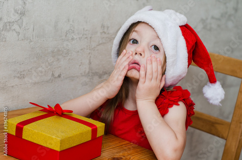 Photography funny little girl grimacing in a Christmas hat with a gift
