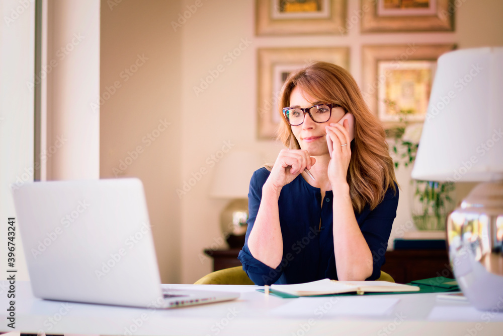 Confident woman using laptop and mobile phone while working from home office Confident woman using laptop and mobile phone while working from home office