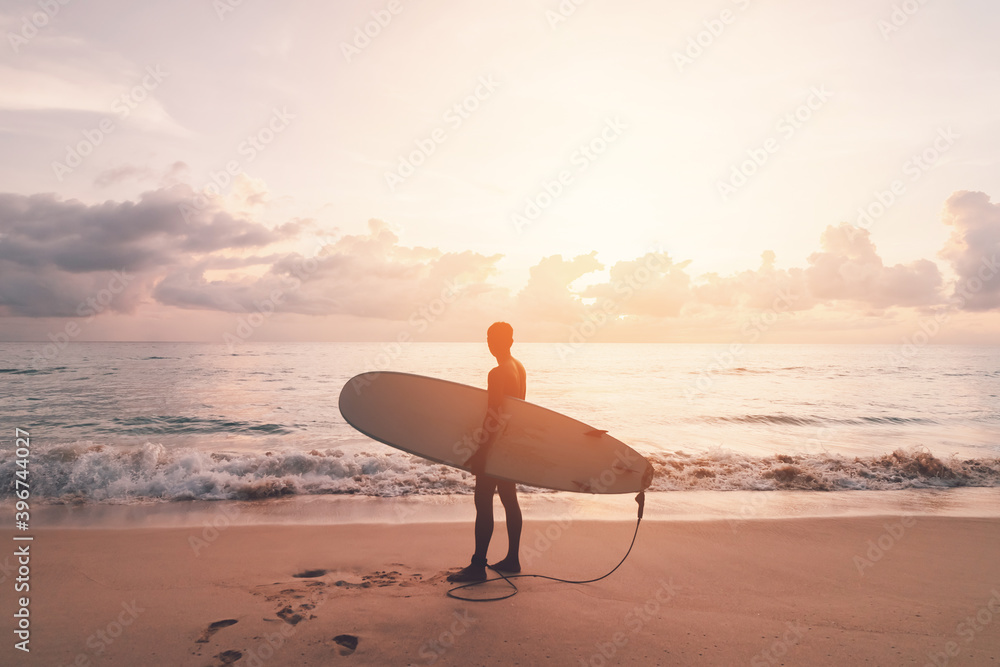 Man hold surfboard standing at tropical sunset beach background. Summer vacation and sport adventrue concept.