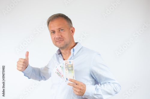 Happy man wearing casual shirt holding money and with thumbs up sign on white background