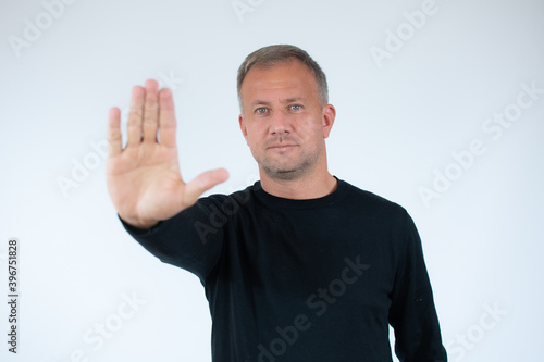 Handsome young man white wall with open hand doing stop sign with serious and confident expression, defense gesture.