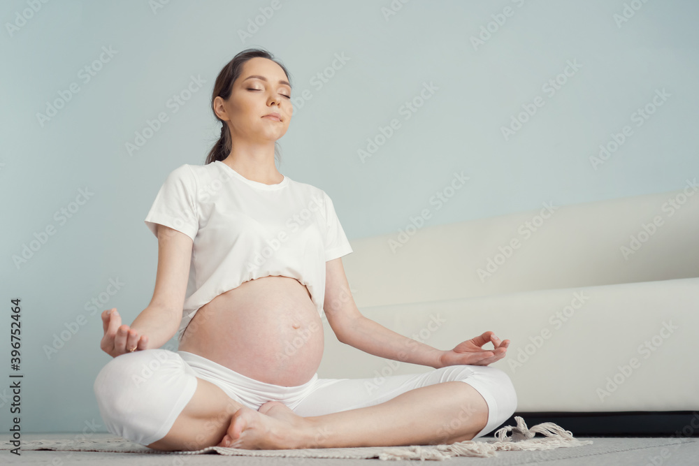 Young pregnant lady with large bare tummy meditates sitting in lotus position on floor at home close-up copyspace Young pregnant lady with large bare tummy meditates sitting in lotus position on floor at home close-up copyspace