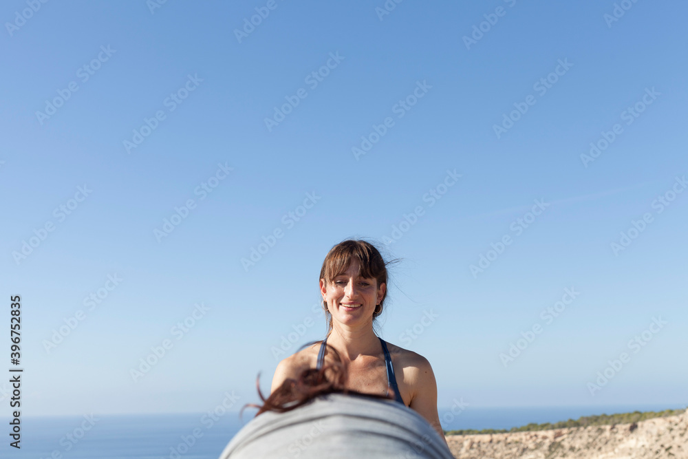 A yoga teacher teaching her student on the top of a cliff. The teacher corrects and teaches yoga poses to the student