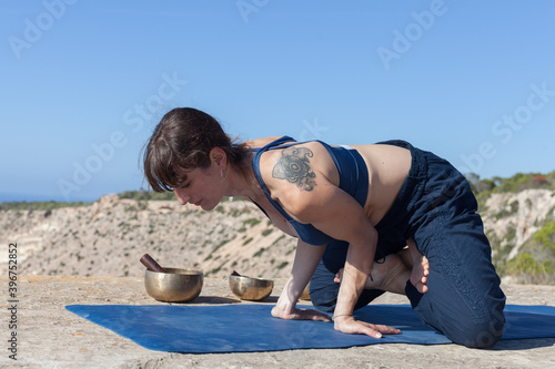 A yoga teacher teaching her student on the top of a cliff. The teacher corrects and teaches yoga poses to the student