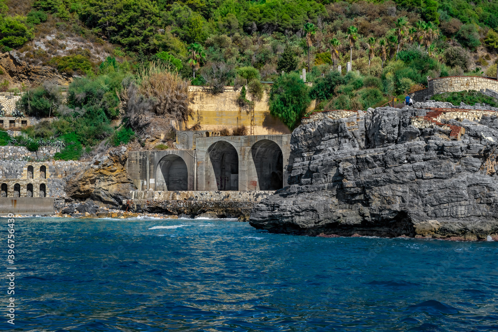 View from Mediterranean Sea to an abandoned Emirgan Ulas Mesire Yeri park and a flooded Ulas beach with large arched gate in a stone wall in Alanya (Turkey). Seascape of the Turkish Riviera coastline