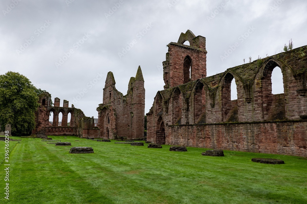 Red brick ruins of medieval Arbroath Abbey and courtyard in Scotland in cloudy weather