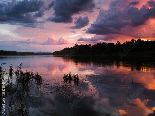 Landscape with river, clouds, water grass and mountain in distance at sunset. Dramatic riverine scene during cloudy dusk with last sun glow in clouds © slobodan