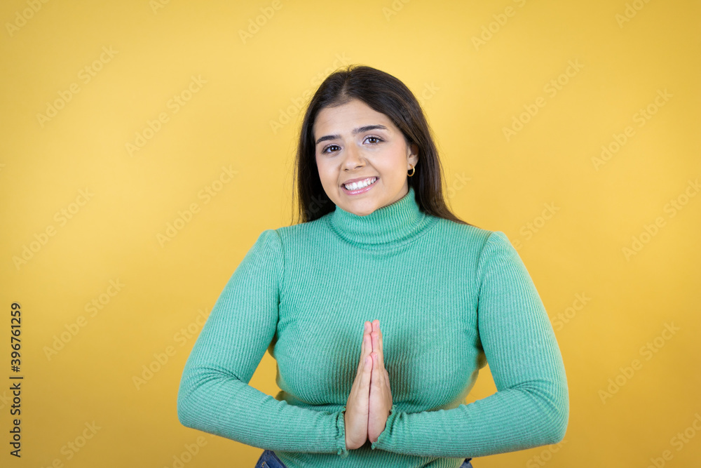 Fototapeta premium Young caucasian woman over isolated yellow background begging and praying with hands together with hope expression on face very emotional and worried