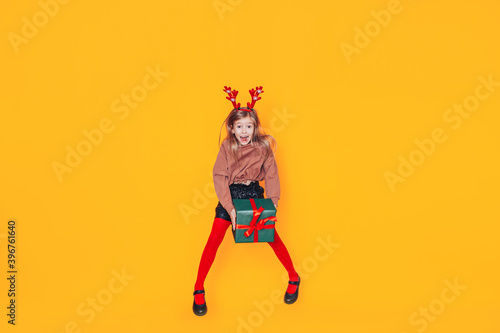 Child holding a box in green packaging with a gift. Christmas mood. She has antlers on her head