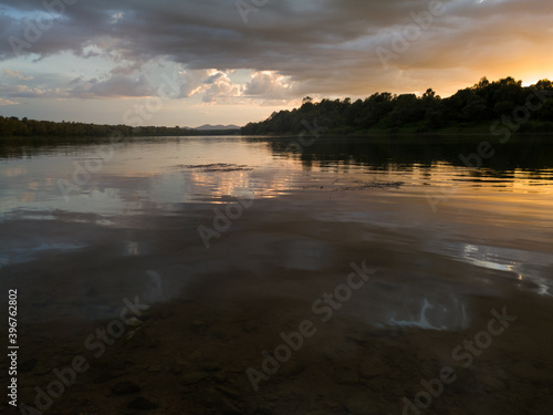 Landscape with river  clouds and mountains in distance at sunset with sun glow in clouds. Peaceful riverine scene during cloudy evening.