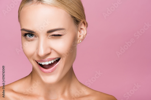 beautiful blonde woman with perfect skin winking isolated on pink photo