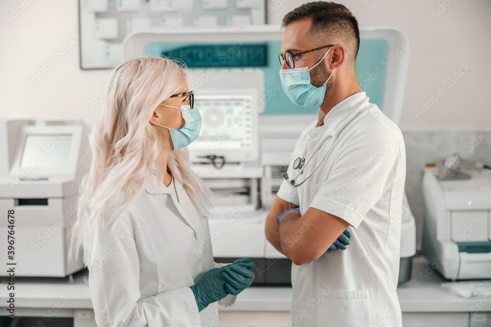 Two dedicated lab assistants standing in laboratory and talking about new cure for corona virus. Two dedicated lab assistants standing in laboratory and talking about new cure for corona virus.